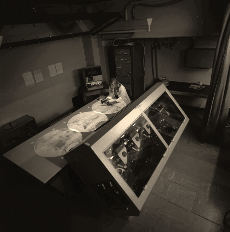 Image en noir et blanc, une femme en blouse blanche inspecte avec attention les clichés obtenus par Gargamelle