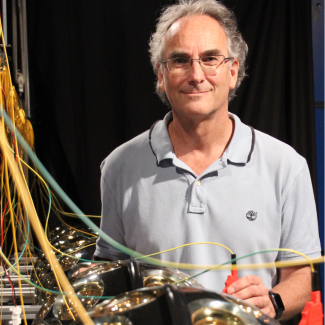 Portrait de Paschal Coyle. Il se tient à droite d'une rangée de détecteurs de neutrinos.