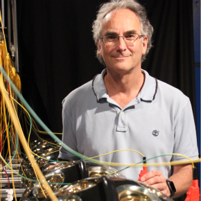 Portrait de Paschal Coyle. Il se tient à droite d'une rangée de détecteurs de neutrinos.